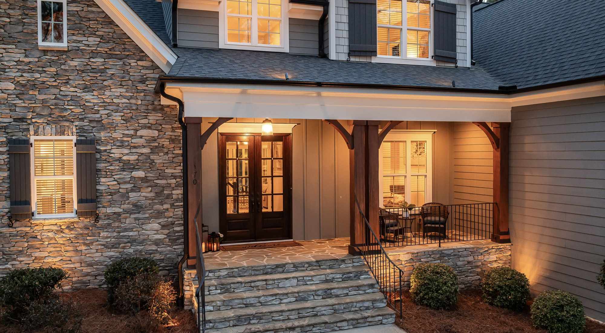 An inviting covered front porch with a stone facade on a family home at golden hour